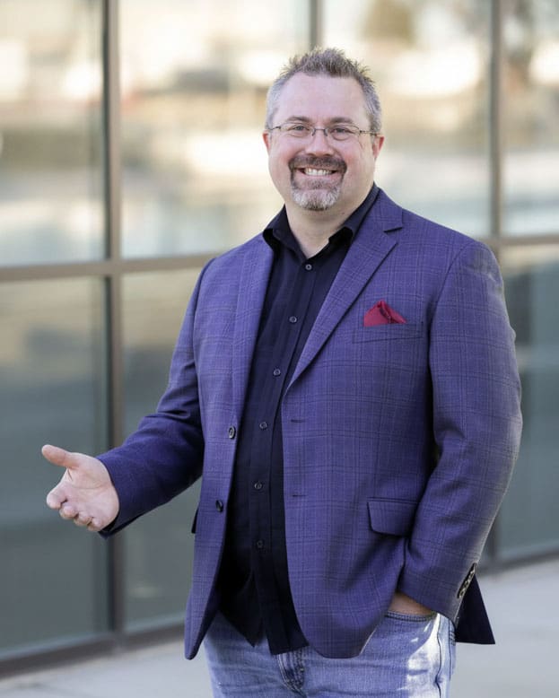 Smiling Realtor Don Enos in a blue blazer standing outside a modern building
